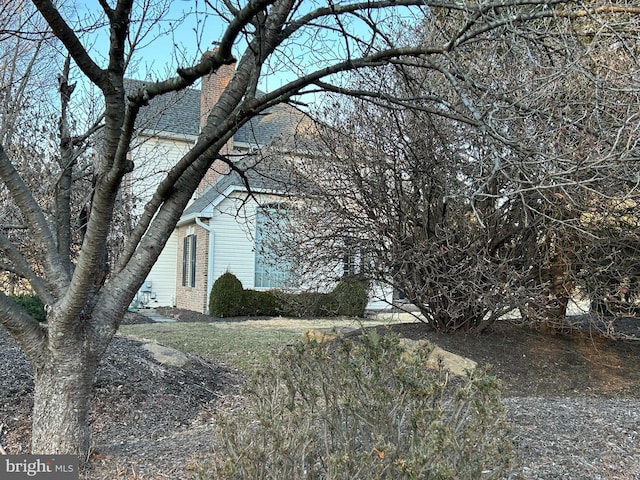 view of home's exterior featuring brick siding, a chimney, and roof with shingles