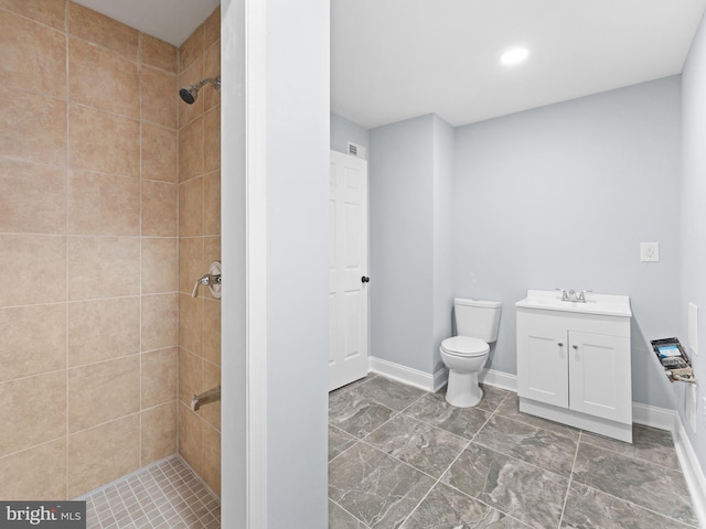 bathroom featuring vanity, a tile shower, and toilet