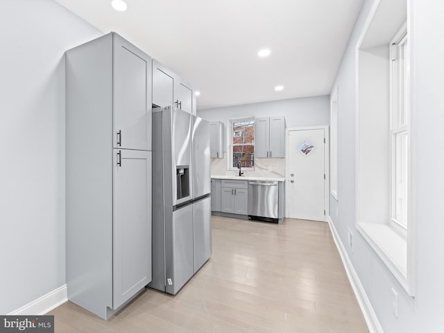 kitchen with sink, gray cabinetry, light hardwood / wood-style flooring, appliances with stainless steel finishes, and backsplash