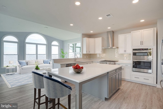 kitchen featuring white cabinetry, a center island, wall chimney exhaust hood, and appliances with stainless steel finishes