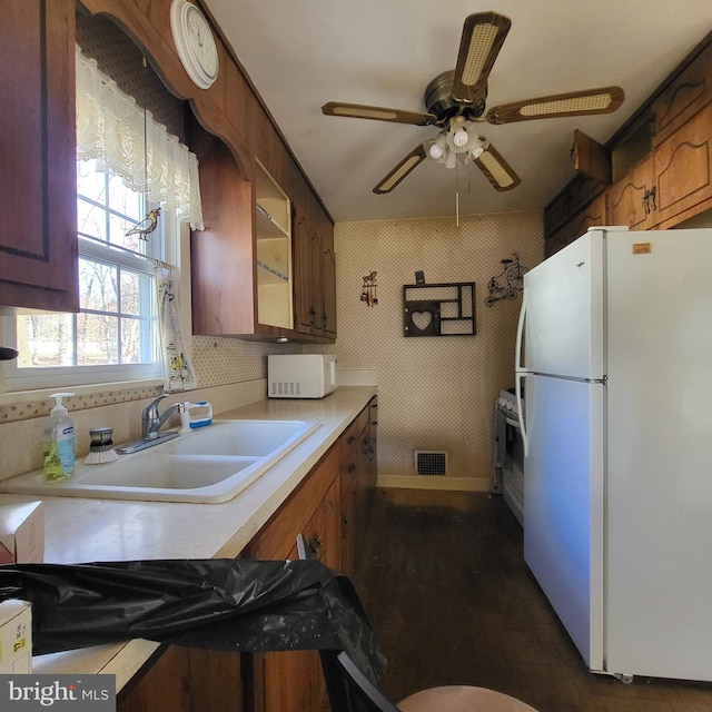 kitchen with light countertops, visible vents, brown cabinetry, a sink, and white appliances