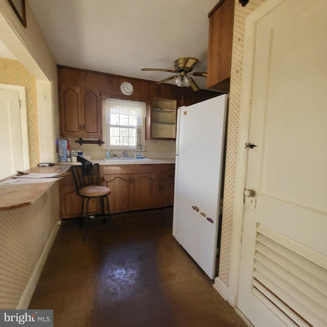 kitchen featuring brown cabinetry, ceiling fan, freestanding refrigerator, light countertops, and a sink