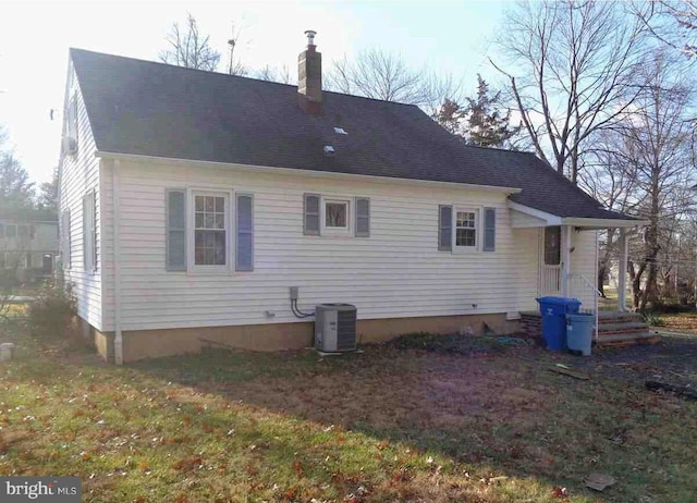 back of house featuring roof with shingles, a lawn, a chimney, and central AC unit