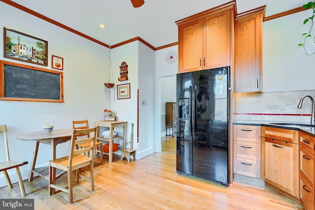 kitchen with light wood finished floors, a sink, decorative backsplash, crown molding, and black fridge