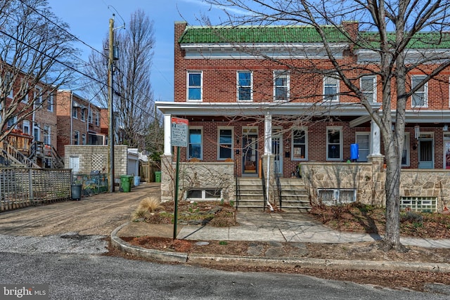 townhome / multi-family property featuring a tile roof, brick siding, a porch, and fence