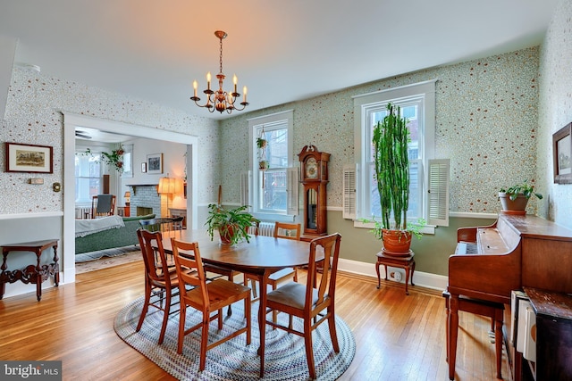 dining area with wallpapered walls, baseboards, a fireplace, an inviting chandelier, and light wood-style floors