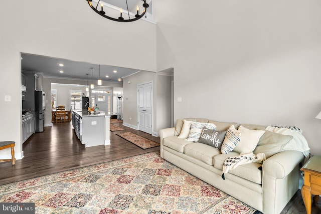 living room featuring dark hardwood / wood-style flooring, a towering ceiling, ornamental molding, and an inviting chandelier