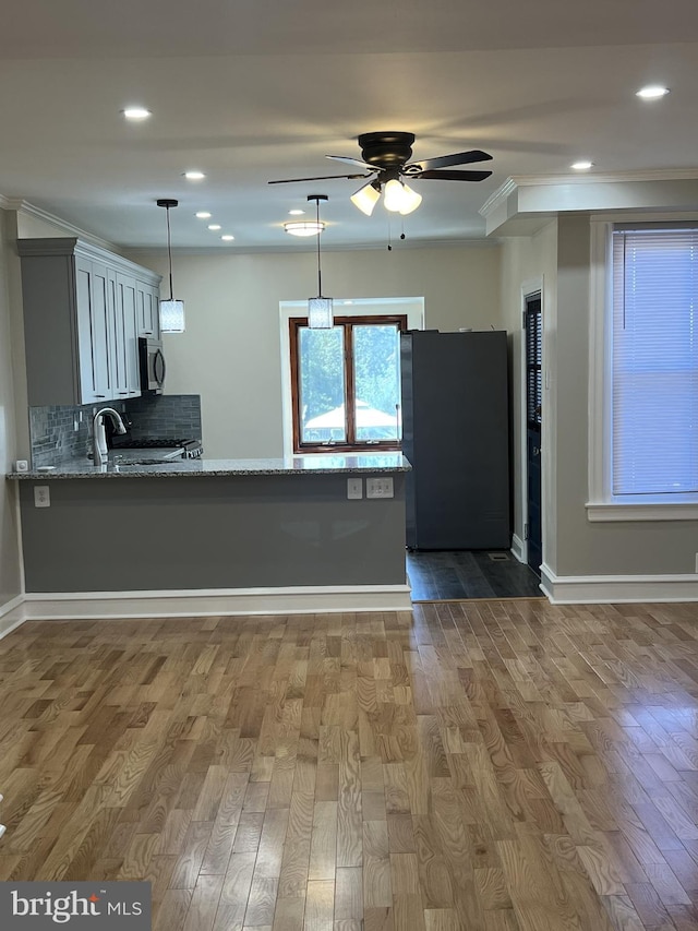 kitchen with stainless steel appliances, hardwood / wood-style flooring, light stone counters, and kitchen peninsula