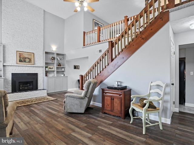 living room with a fireplace, dark wood-type flooring, ceiling fan, and a high ceiling