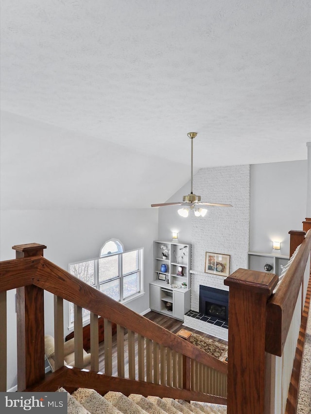 stairway with ceiling fan, a fireplace, vaulted ceiling, and hardwood / wood-style floors