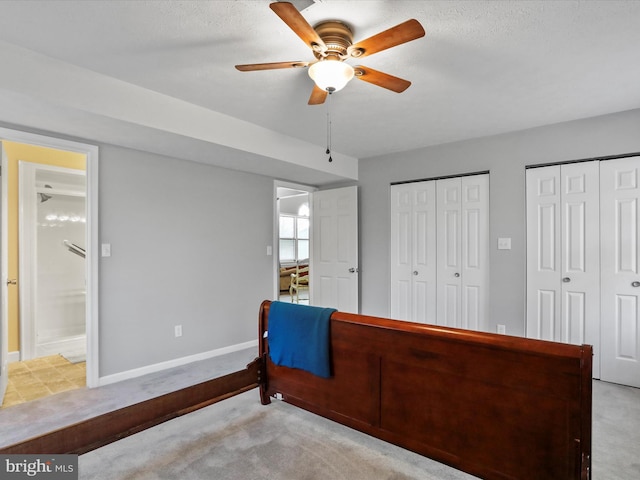 bedroom featuring ensuite bathroom, two closets, light colored carpet, and ceiling fan