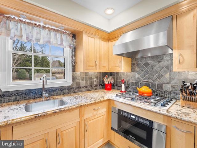 kitchen featuring light brown cabinetry, stainless steel gas stovetop, sink, wall oven, and wall chimney range hood