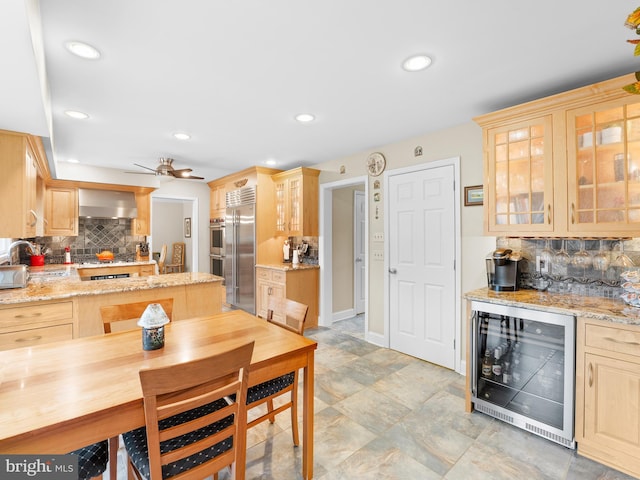 kitchen featuring wine cooler, light stone countertops, wall chimney exhaust hood, and appliances with stainless steel finishes