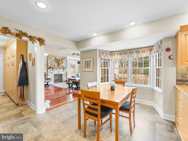 tiled dining room with ceiling fan and a fireplace