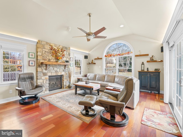 living room featuring lofted ceiling, a healthy amount of sunlight, a stone fireplace, and light hardwood / wood-style flooring