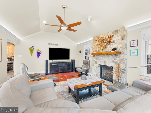 living room featuring a stone fireplace, wood-type flooring, lofted ceiling, wine cooler, and ornamental molding