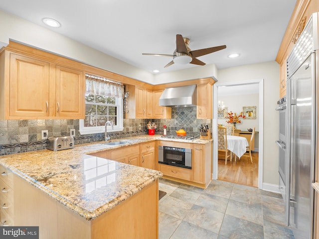 kitchen featuring light brown cabinetry, wall chimney range hood, sink, and appliances with stainless steel finishes