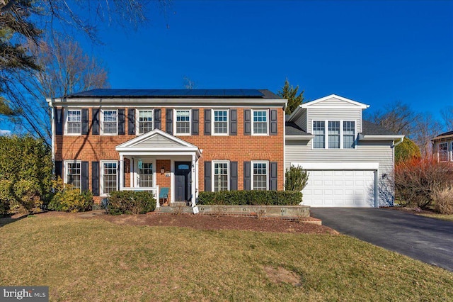 colonial inspired home with a front lawn, aphalt driveway, solar panels, and brick siding