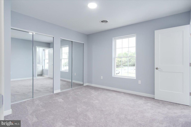 unfurnished bedroom with multiple closets and light colored carpet