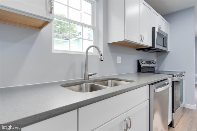 kitchen with stainless steel appliances, sink, white cabinets, and light hardwood / wood-style floors