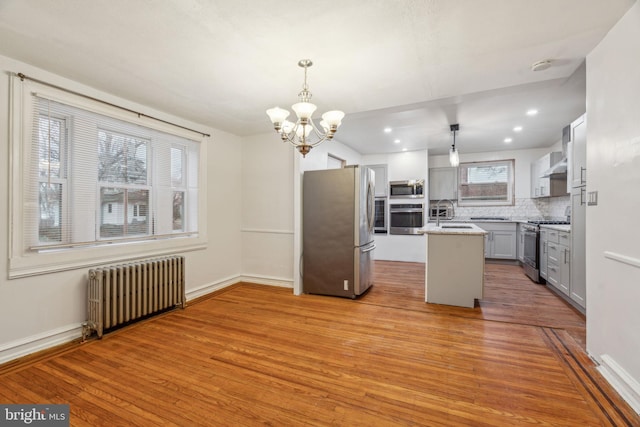 kitchen featuring gray cabinetry, hanging light fixtures, radiator, a kitchen island, and stainless steel appliances