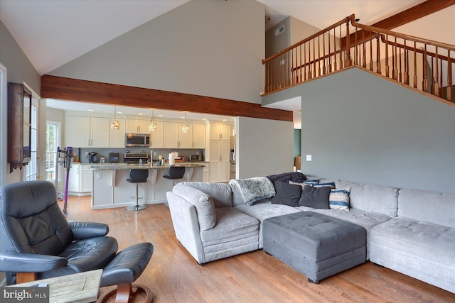 living room with high vaulted ceiling, light wood finished floors, stairway, and visible vents