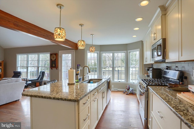 kitchen with appliances with stainless steel finishes, open floor plan, decorative light fixtures, a kitchen island with sink, and a sink