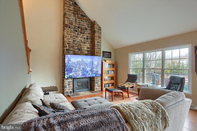 living room featuring light wood finished floors, high vaulted ceiling, a stone fireplace, and plenty of natural light