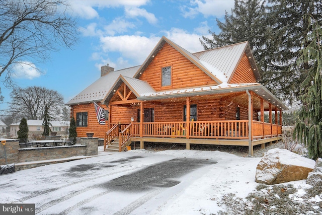 view of front of property featuring a chimney, covered porch, log exterior, and metal roof