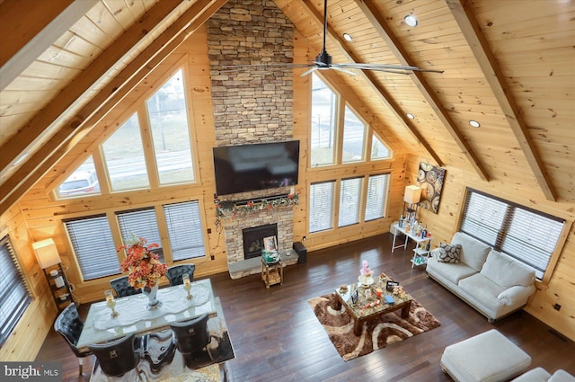 living area featuring hardwood / wood-style floors, a stone fireplace, wood walls, wooden ceiling, and beamed ceiling