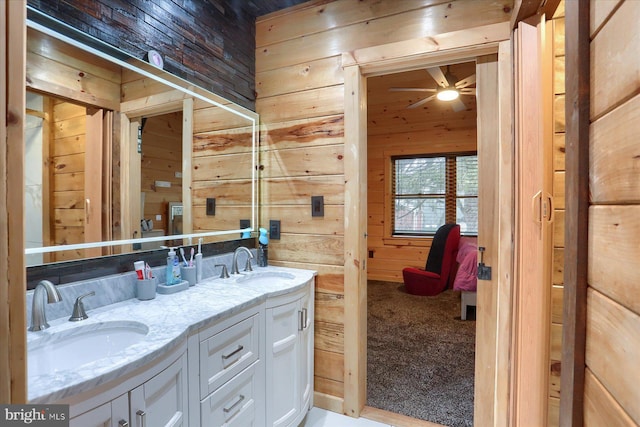 bathroom featuring ceiling fan, double vanity, wooden walls, and a sink