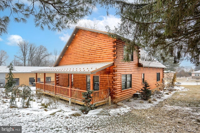 view of snow covered exterior with a porch, log exterior, and metal roof