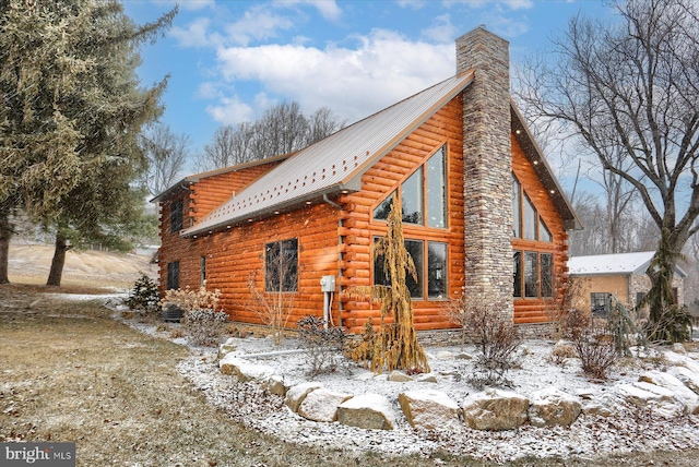 view of snow covered exterior featuring log exterior, a chimney, and metal roof