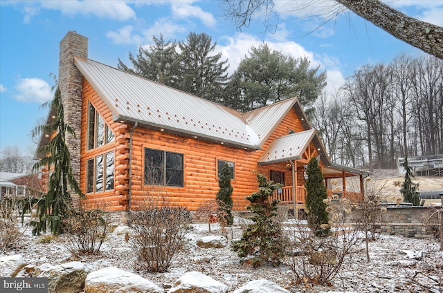 exterior space with log siding, metal roof, covered porch, and a chimney