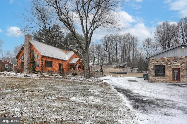 view of snow covered exterior with a chimney, stone siding, log exterior, and metal roof