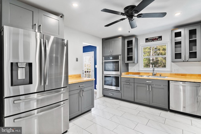 kitchen with wood counters, glass insert cabinets, marble finish floor, stainless steel appliances, and a sink