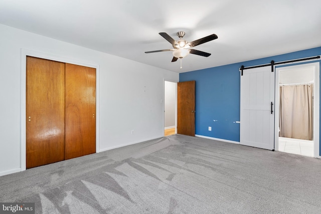 unfurnished bedroom featuring a barn door, baseboards, a ceiling fan, carpet flooring, and a closet