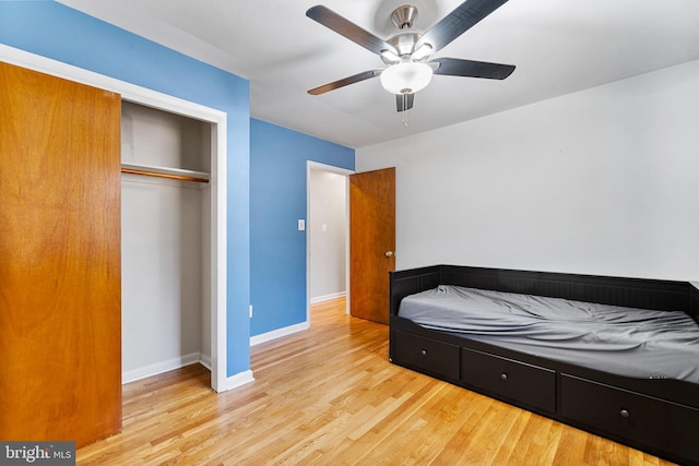 bedroom with light wood finished floors, ceiling fan, baseboards, and a closet