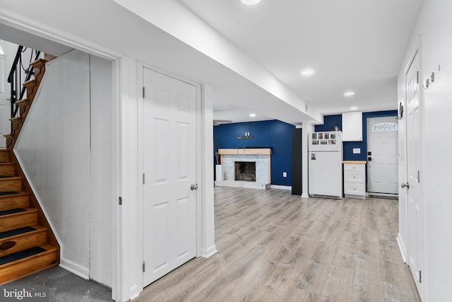 interior space with baseboards, light wood-style floors, freestanding refrigerator, stairs, and a brick fireplace