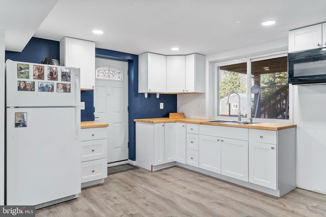 kitchen with black microwave, a sink, wood counters, white cabinetry, and freestanding refrigerator