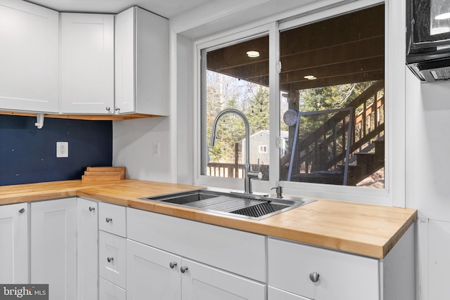 kitchen with butcher block counters, white cabinetry, and a sink