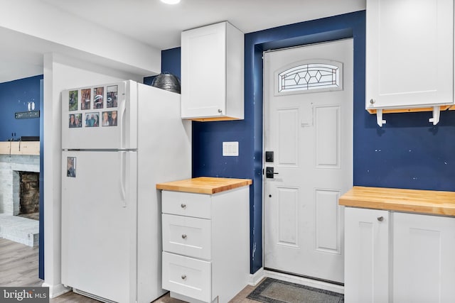 kitchen featuring light wood finished floors, white cabinets, freestanding refrigerator, a brick fireplace, and wooden counters