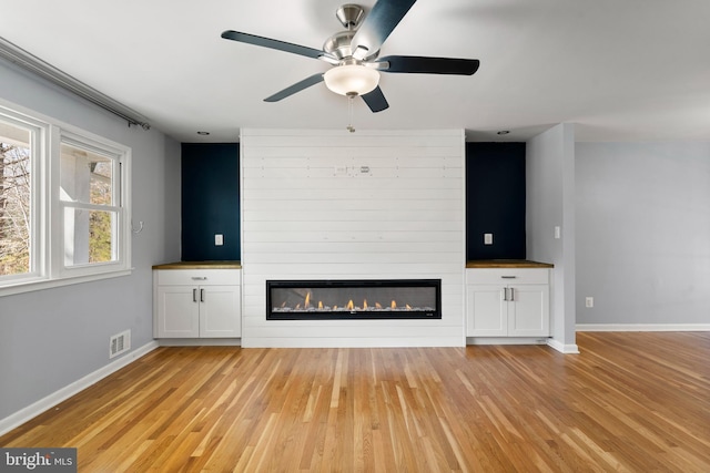 unfurnished living room with a large fireplace, light wood-type flooring, visible vents, and baseboards