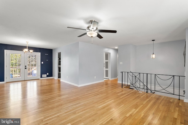 unfurnished room with ceiling fan with notable chandelier, light wood-type flooring, and baseboards