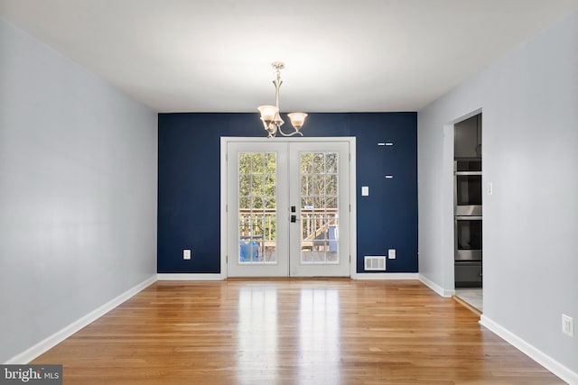 unfurnished dining area with baseboards, visible vents, a chandelier, and wood finished floors