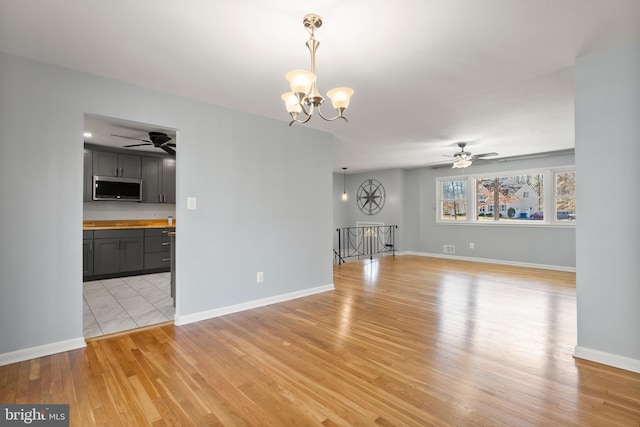 unfurnished living room featuring light wood-style flooring, visible vents, baseboards, and ceiling fan with notable chandelier