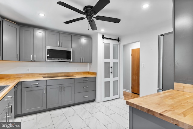 kitchen with butcher block counters, stainless steel microwave, gray cabinets, and a barn door