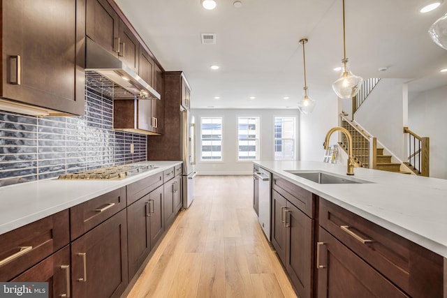 kitchen featuring pendant lighting, sink, light stone counters, stainless steel appliances, and light hardwood / wood-style flooring