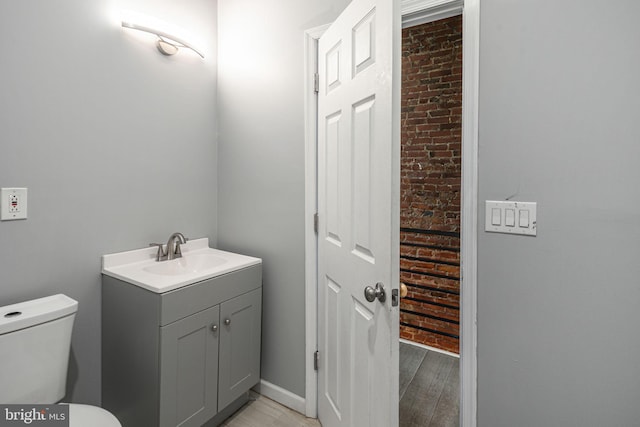 bathroom featuring vanity, brick wall, wood-type flooring, and toilet