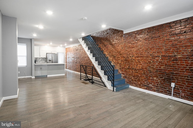 unfurnished living room with crown molding, dark hardwood / wood-style floors, and brick wall